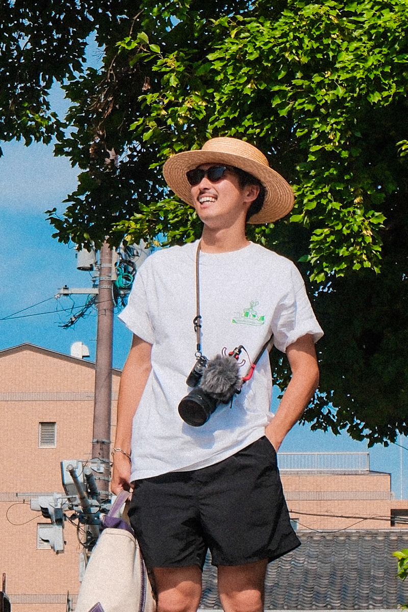 カメラを首から下げ、麦わら帽子をかぶって笑うKoseの写真